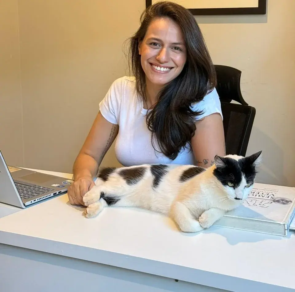 Dra. Mariana Neves sorrindo à mesa, com um gato deitado ao lado